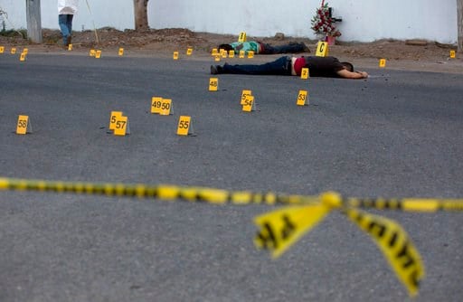 FILE - In this June 29, 2017 file photo, investigators mark the spot where spent bullet casing fell next several bodies lying on a road in the town of Navolato, Sinaloa state, Mexico.(AP Photo/Enric Marti, File)